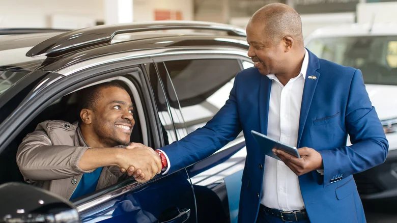 Happy buyer shaking hands with a dealer in his new car