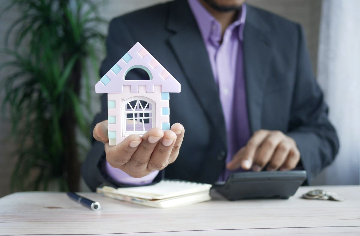 Credit consultant holding a model home while calculating a home loan plan